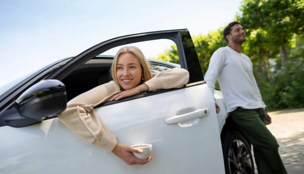 Una donna seduta in macchina con una tazzina di caffè in mano e un ragazzo in piedi