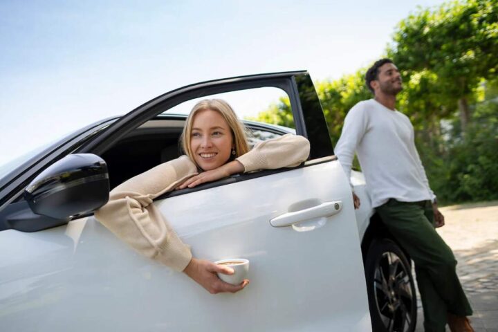 Una donna seduta in macchina con una tazzina di caffè in mano e un ragazzo in piedi
