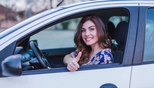 Una ragazza seduta in auto sorride e fa il segno del pollice su