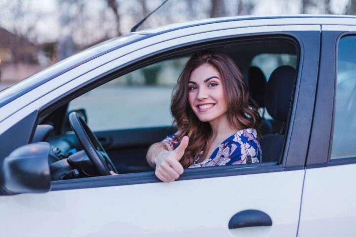 Una ragazza seduta in auto sorride e fa il segno del pollice su 