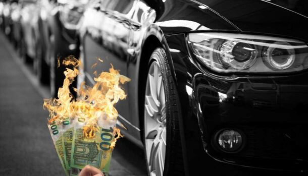 Delle auto e una mano che stringe delle banconote in fiamme