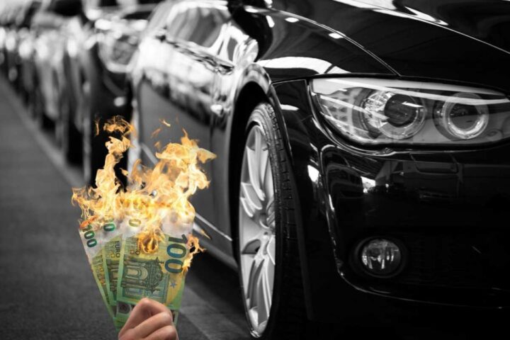 Delle auto e una mano che stringe delle banconote in fiamme